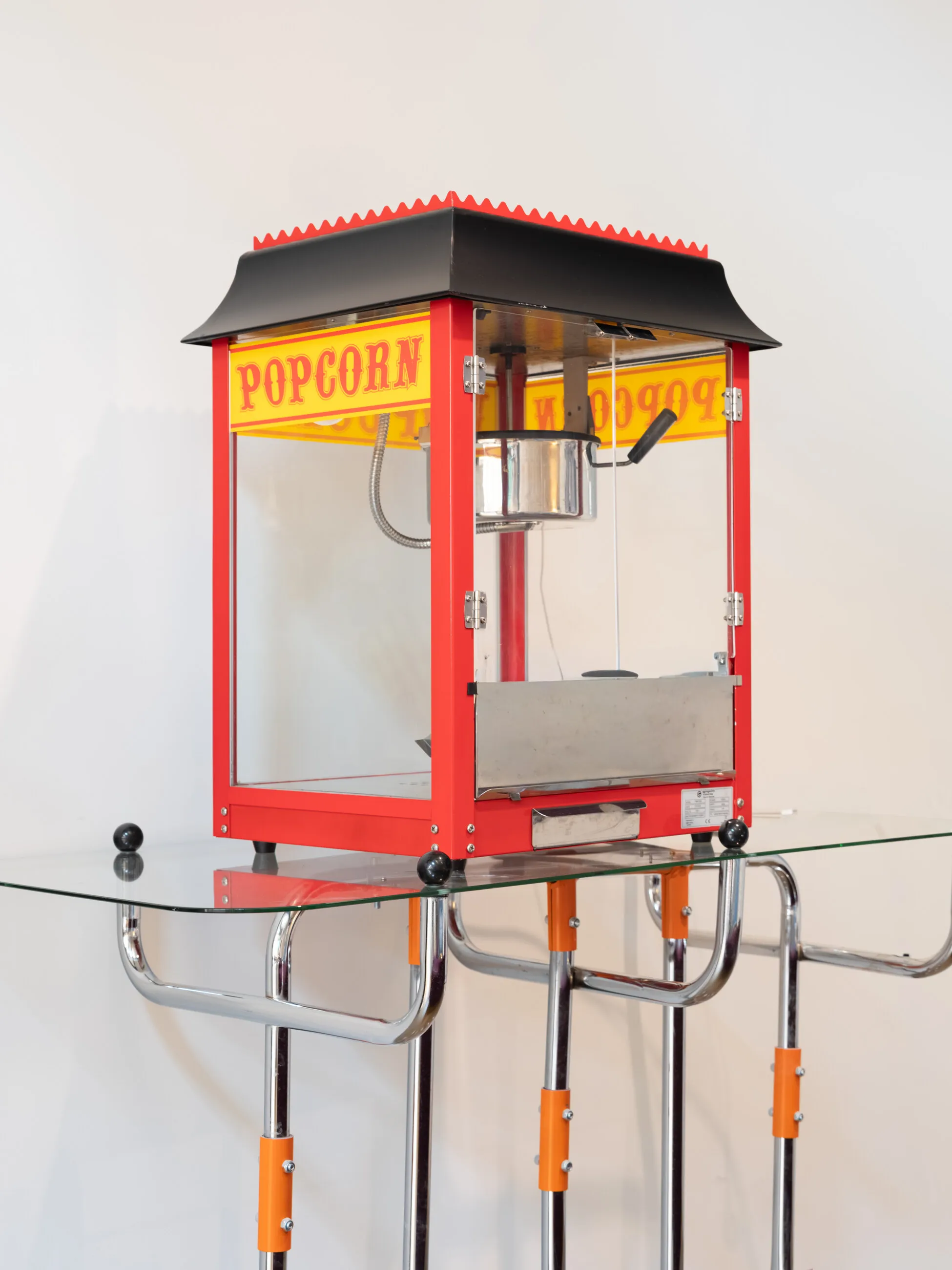 Raudonas „Popcorn“ aparatas ant stiklinio staliuko poilsio zonoje